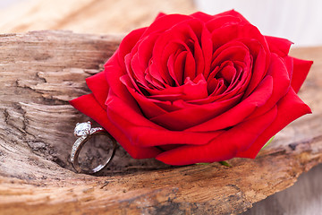 Image showing beautiful ring on wooden background and red rose