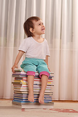 Image showing Little Caucasian girl sitting on a pile of books