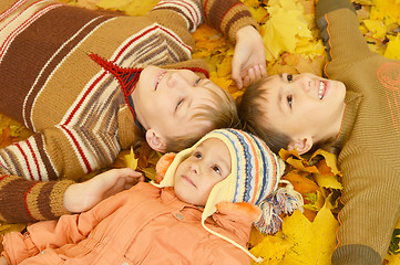 Image showing Family of three lying on yellow leaves
