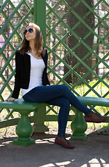 Image showing portrait of the beautiful girl sits on a bench in green park