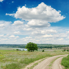 Image showing dirty road in green meadow and clouds over it