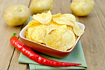 Image showing Chips in a bowl with hot peppers and potatoes on board