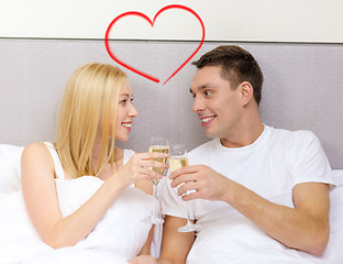 Image showing smiling couple with champagne glasses in bed