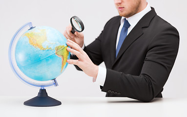 Image showing businessman hand holding magnifier over globe