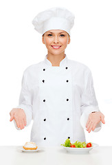 Image showing smiling female chef with salad and cake on plates