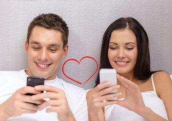 Image showing smiling couple in bed with smartphones