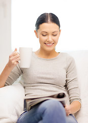 Image showing woman with cup of coffee reading magazine at home