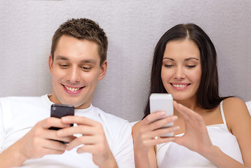 Image showing smiling couple in bed with smartphones