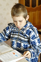 Image showing The 10-year-old boy sits with the textbook, doing homework.