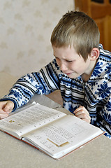 Image showing The 10-year-old boy with tears in the eyes sits before the textb