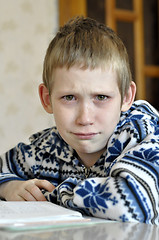 Image showing The 10-year-old boy with tears in the eyes sits before the textb