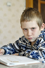 Image showing The 10-year-old boy with tears in the eyes sits before the textb