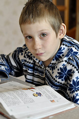 Image showing The 10-year-old boy with tears in the eyes sits before the textb