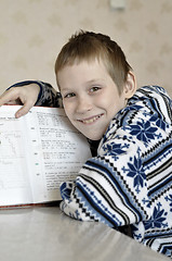 Image showing The 10-year-old boy sits with the textbook, doing homework.