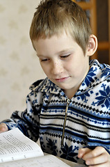 Image showing The 10-year-old boy sits with the textbook, doing homework.