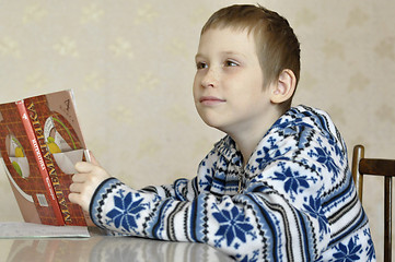 Image showing The 10-year-old boy sits with the textbook, doing homework.