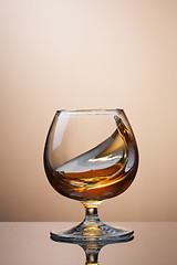 Image showing Splash of cognac in glass on brown background