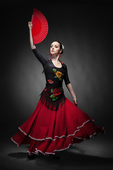 Image showing young woman dancing flamenco with fan on black