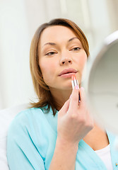 Image showing woman applying lipstick and holding mirror