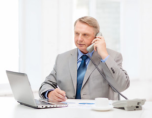 Image showing busy older businessman with laptop and telephone
