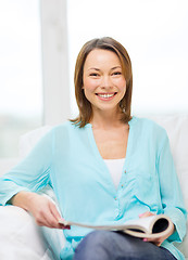 Image showing smiling woman reading magazine at home