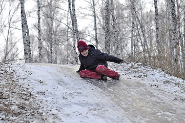 Image showing the teenage boy rides from a hill in the snow-covered wood.