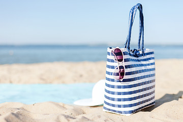 Image showing straw hat, sunglasses and bag lying in the sand