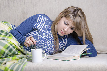 Image showing Girl reading book under a blanket on couch