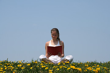 Image showing Young woman reading a book in a flowering field