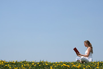 Image showing Young woman reading a book outdoors