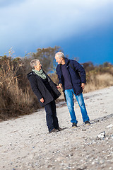 Image showing mature senior couple walking on the beach autumn winter