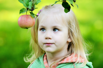 Image showing little girl thoughtfully looks at the apple in garden