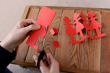 Image showing Cutting a chain of red paper dolls with scissors