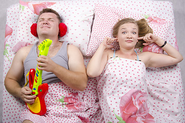 Image showing husband plays guitar, wife covered her fingers in his ears