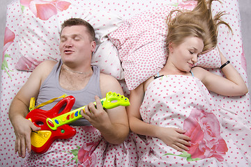 Image showing husband plays  guitar, the wife sleeps