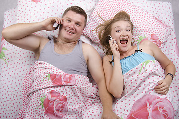 Image showing Young couple talking on the phone lying in bed