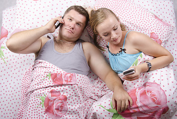 Image showing Young couple talking on the phone lying in bed