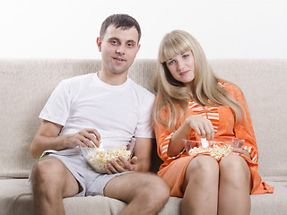 Image showing Young couple sitting on couch, eating popcorn and watching TV