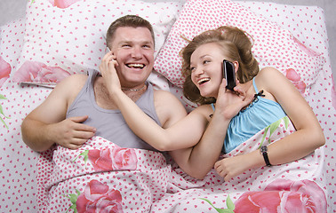Image showing Young couple talking on the phone lying in bed