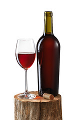 Image showing Glass of red wine and bottle on stump isolated on white