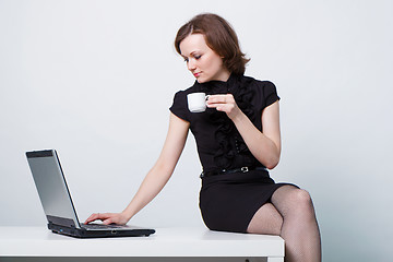 Image showing sitting on the table an girl with a laptop and a cup of coffee