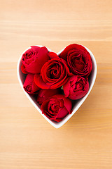 Image showing Red rose inside heart shape bowl on wooden background