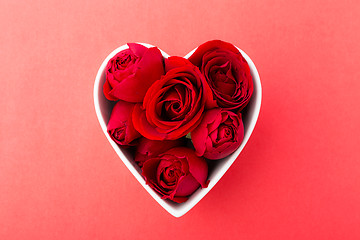 Image showing Red rose inside heart shape bowl on red background