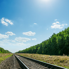 Image showing railroad to horizon in green landscape and blue sky with sun ove