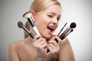 Image showing Young smiling woman with make up brushes on white