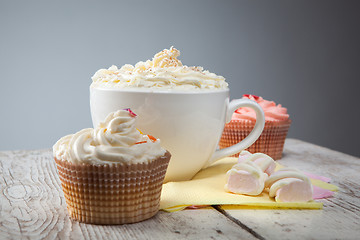 Image showing hot chocolate with marshmallows, cream and cupcakes on wooden ba