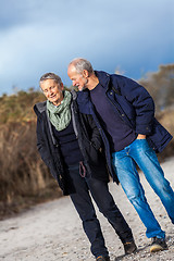 Image showing mature senior couple walking on the beach autumn winter