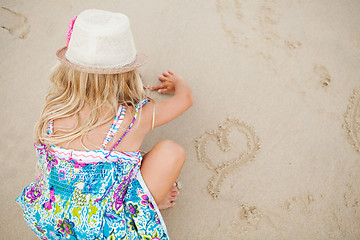 Image showing Young girl drawing heart shapes in sand