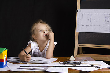 Image showing Girl-architect sitting behind a Desk and thought dreamily