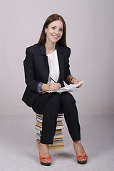 Image showing School teacher sitting on books checks notebooks students